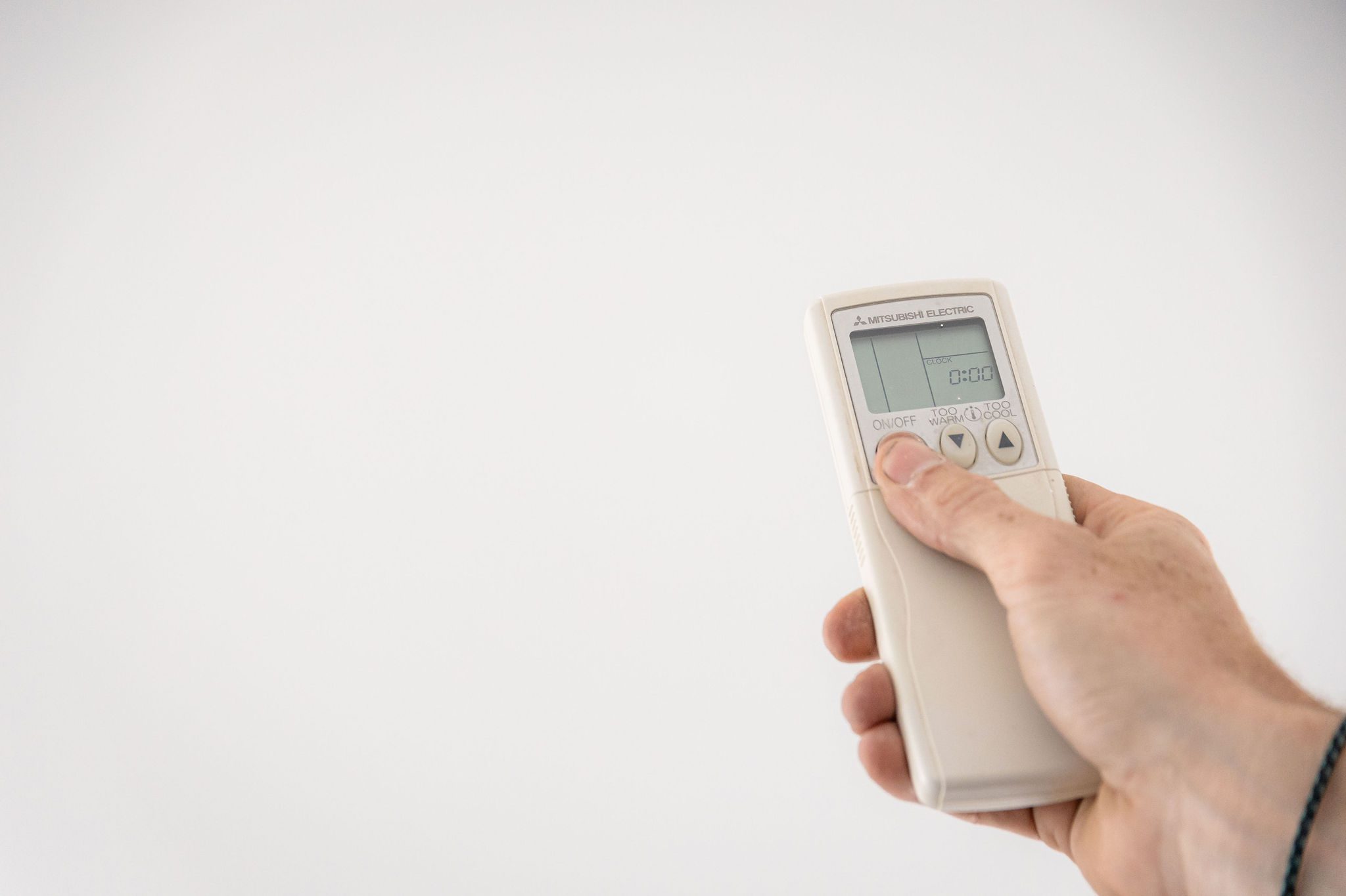 A hand holds a remote control, pressing the on/off button.