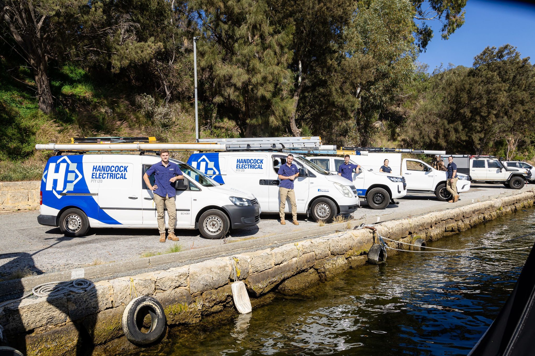 A team of electricians in Perth from Handcock Electrical standing next to their fully equipped service vehicles, ready to provide professional electrical services.